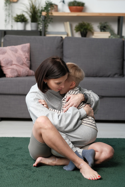 A woman with short dark hair dressed in a light sportswear hugging her little son on a green carpet