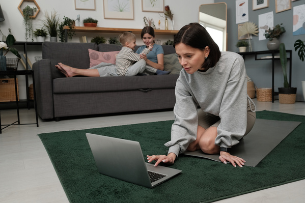 A woman with dark hair going to do yoga online at home while her daughter entertaining her brother
