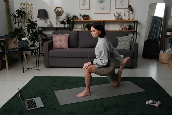 A dark-haired woman practicing online yoga classes in a living room on a green carpet