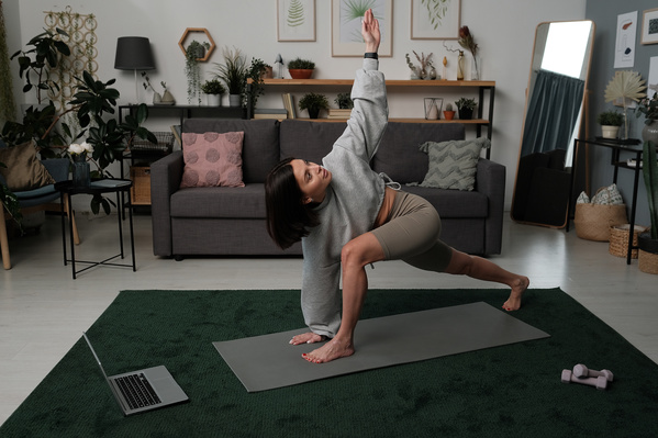 A beautiful woman with short dark hair dressed in a light sportswear doing yoga online on a gray sports mat