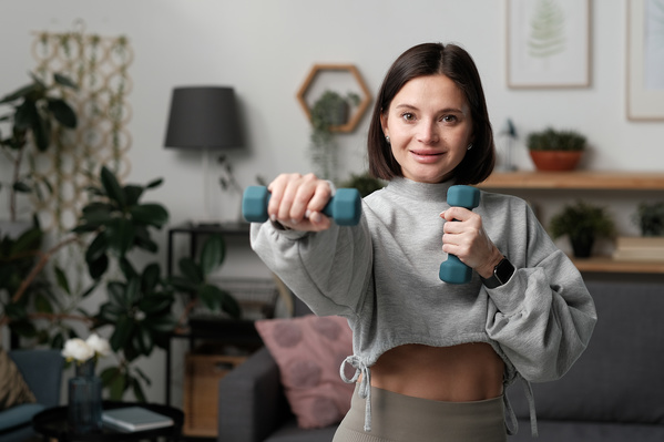 A dark-haired woman in a gray sports top performing an exercise with dumbbells to train her hands