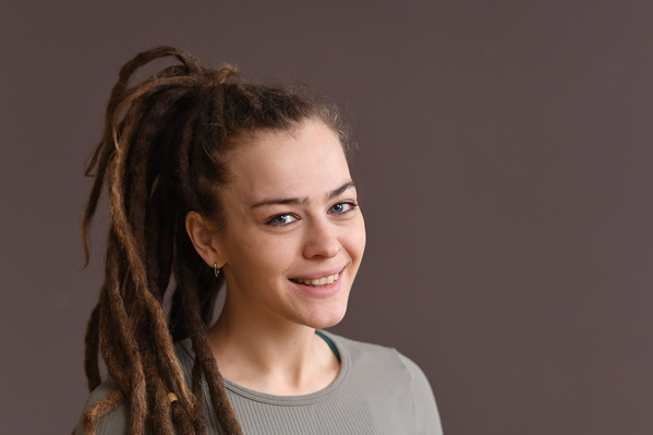 Portrait of a broadly smiling woman with dreadlocks in a beige sports top on a beige background