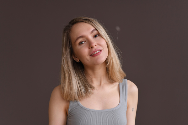 A smiling sporty woman with blonde hair in a gray sports top against a beige background
