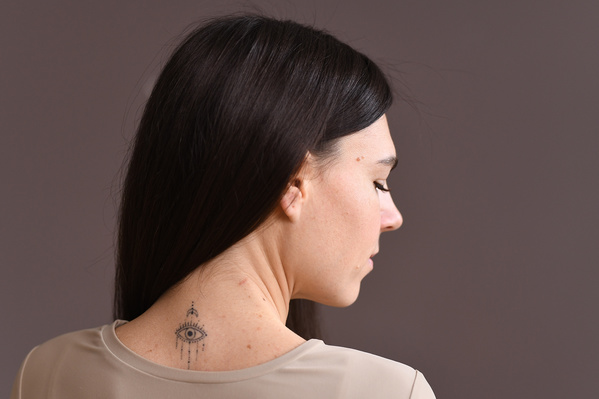 Close-up of a dark-haired athletic woman with a tattoo on her neck from the back against a beige background