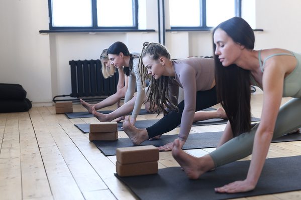 Women in leggings stretching their legs on black yoga mats