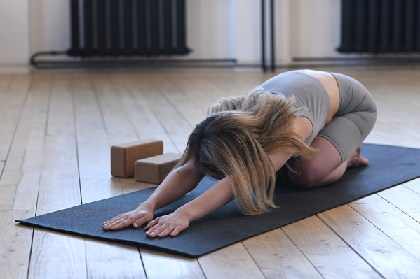 A woman with short blond hair in gray sportswear in a balasana pose on a black yoga mat