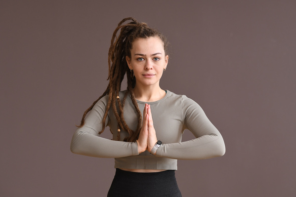 A beautiful woman with tidied up dreadlocks dressed in a gray sports top doing a praying mudra with her hands