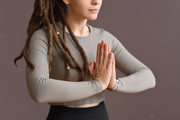 A woman with tidied up dreadlocks dressed in a gray sports top performing a praying mudra