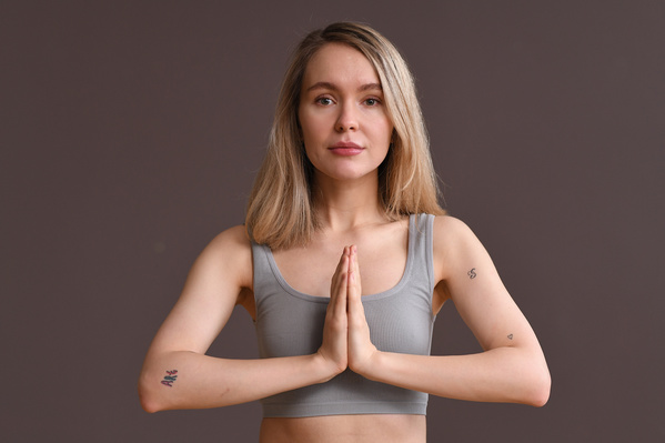 A woman with short blond hair dressed in a light top looking to the side folded her hands in a praying mudra