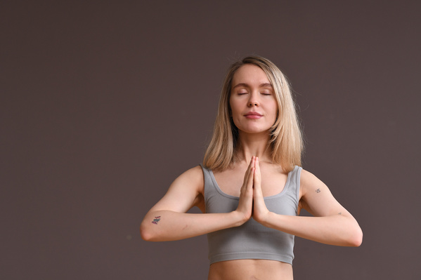 A woman with blonde loose hair dressed in a gray top closed her eyes and doing anjali mudra