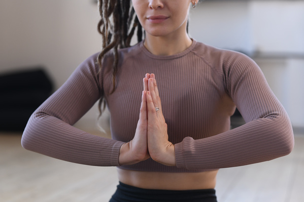 A woman with tidied up dreadlocks in a brown top folded her hands in anjali mudra