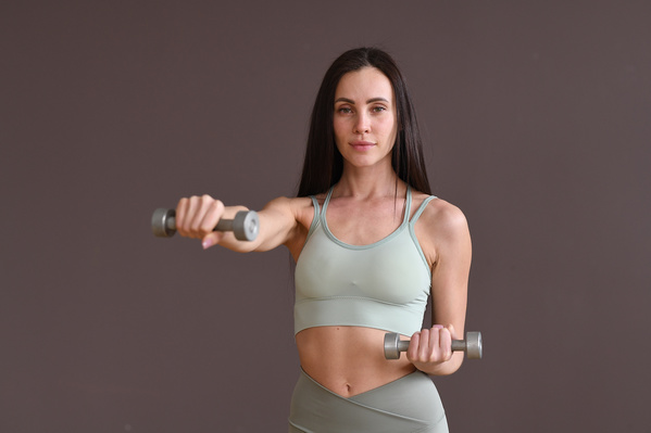 A woman with dark long hair in gray sports clothes pumping her arms using dumbbells