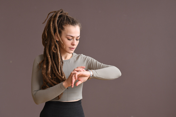 A woman with tidied up dreadlocks wearing in a beige sports top looking at a wrist sports watch
