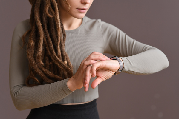 A woman with dreadlocks dressed in a gray sports top looking at a silver fitness tracker