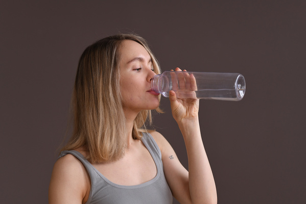 A woman with short blond hair drinking water from a transparent plastic sports bottle