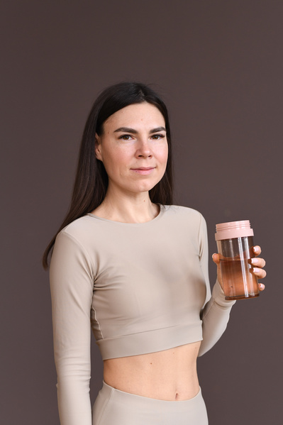A woman with dark hair dressed in a beige sportswear with a pink sports water bottle in her hand