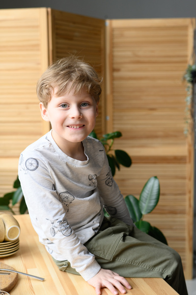 A portrait of a smiling blond boy in a gray longsleeve sitting on a wooden table