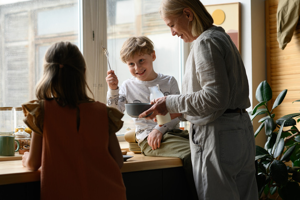 A Boy Making Faces at His Sister and Their Grandmother Cooking Breakfast