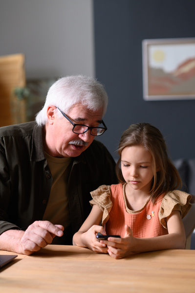 A gray-haired man in a dark shirt talking to his granddaughter using the phone
