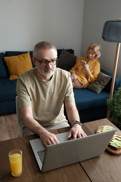A man in glasses working on a silver laptop at breakfast at home