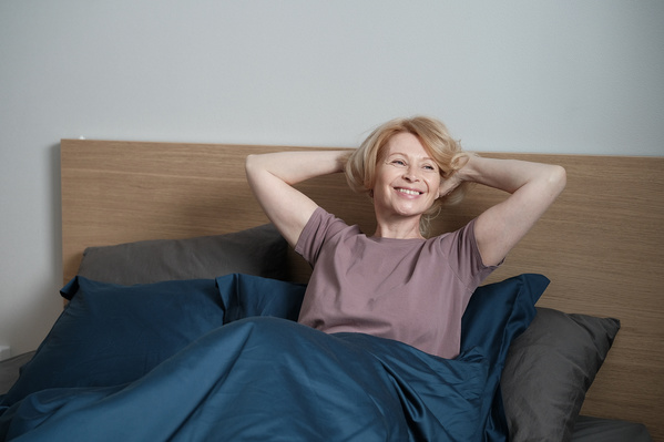 A smiling elderly woman with blonde hair dressed in pajamas enjoying the morning in bed