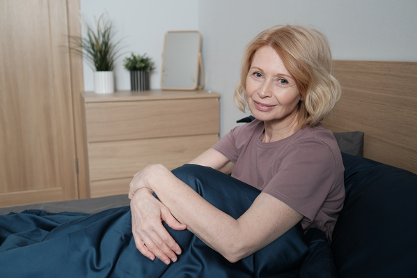 An elderly woman with blonde hair dressed in pajamas sitting in bed in the morning