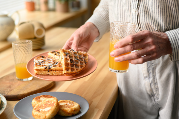 A woman in a light outfit holding a red plate with Viennese waffles and a glass of orange juice for breakfast