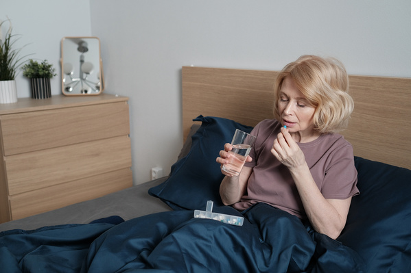 An elderly woman with short blonde hair taking pills sitting in bed in the morning