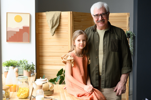 A little girl with brown hair and her grandfather in glasses in the kitchen