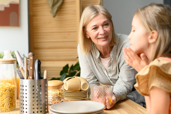 An elderly woman with short blonde hair dressed in light clothes talking to her little granddaughter