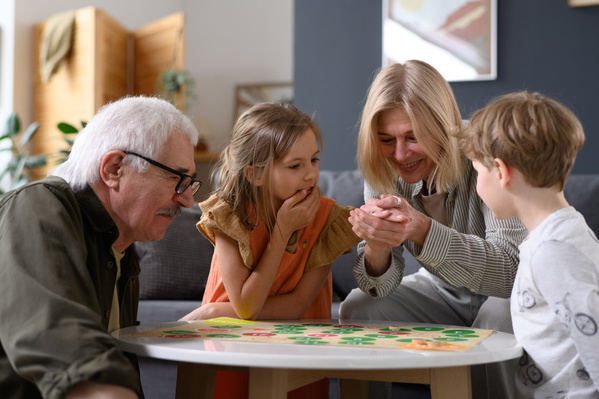 A grandmother throwing a dice during a board game with her little grandchildren and a gray-haired husband