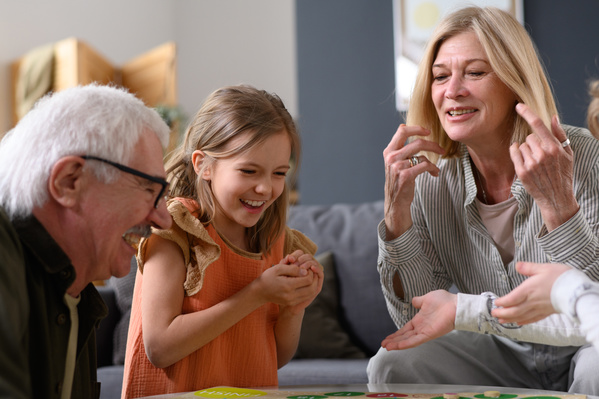 A brown-haired girl playing a board game with her laughing grandparents