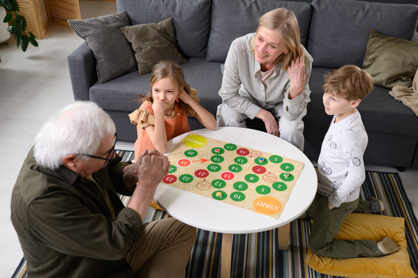 Elderly grandparents playing a bright board game with their little grandchildren in a bright living room