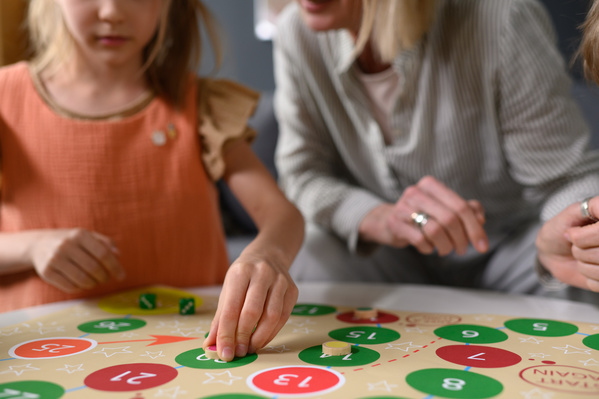 A little girl in bright clothes making a move during a board game with her family