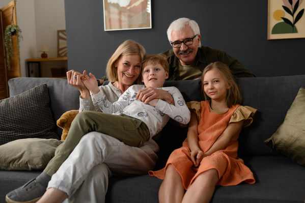 Family photo of smiling elderly grandparents with blond hair and their grandchildren sitting on a dark sofa