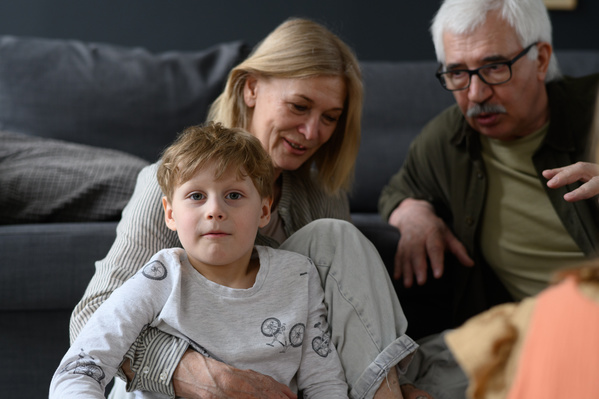 A blond-haired boy sitting with his elderly grandparents chatting with each other in a bright room