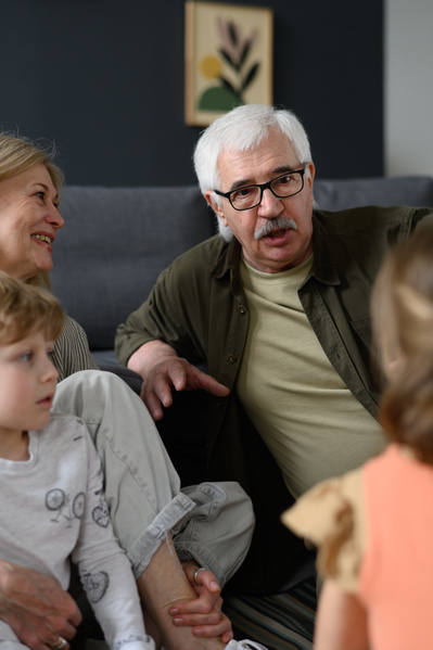 A gray-haired man with glasses talking to his little grandchildren and an elderly wife