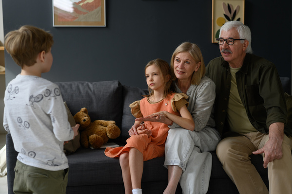 A blond-haired boy telling a story to his elderly grandparents and younger sister