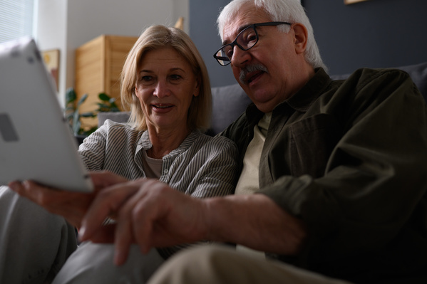 An elderly man and a woman with blonde hair using a tablet at home