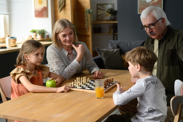 A grandparents with blond hair watching their little grandchildren playing chess game