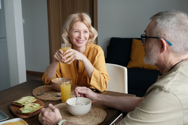 An elderly smiling wife with blonde hair having breakfast with her husband in a bright kitchen