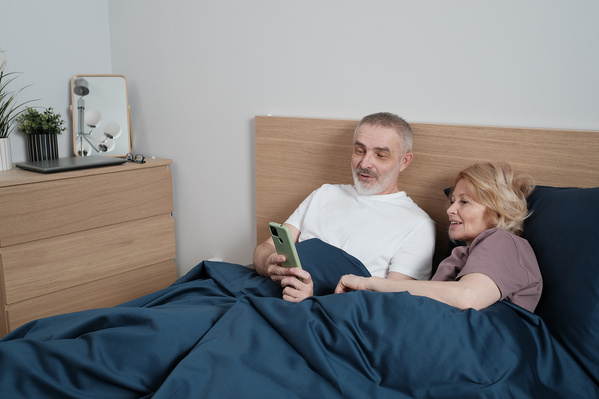 An elderly couple with blonde hair using a phone before going to bed
