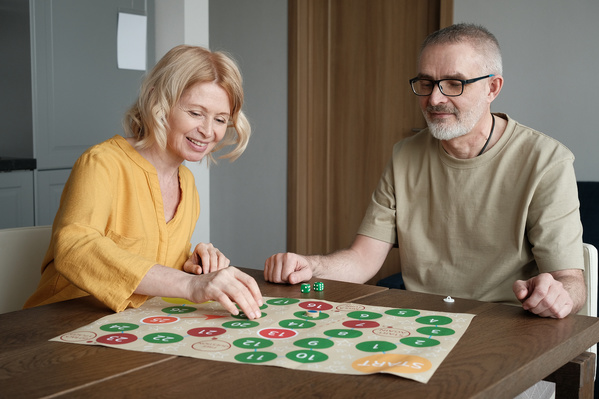 An elderly smiling woman with blonde hair and her husband in a light T-shirt playing a bright board game