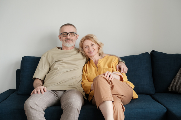 An elderly couple in light outfits sitting in an embrace on a dark blue sofa