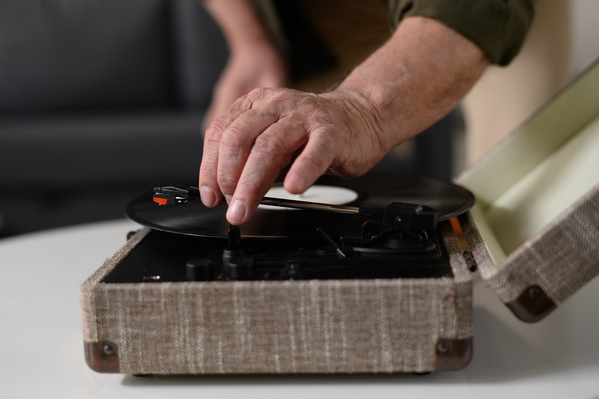 An aged man in a dark shirt putting a vinyl record into a player