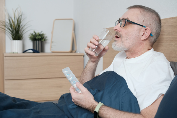 An elderly man in glasses taking daily medications in bed