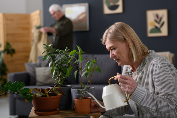 An elderly woman with short blonde hair watering potted houseplants