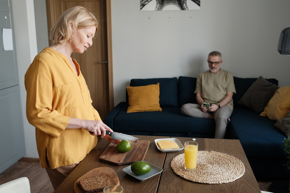 An elderly woman with short blonde hair dressed in a yellow outfit slicing avocado for breakfast