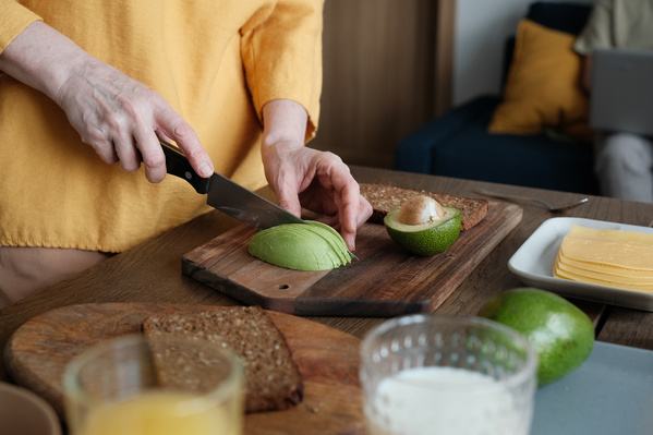 A woman in a yellow blouse cutting avocado for toasts for breakfast