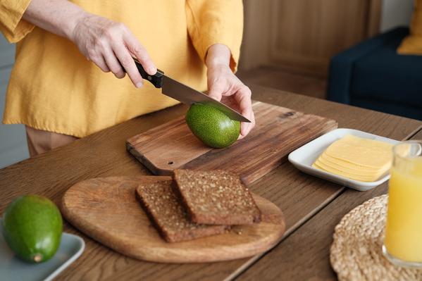 A woman in a yellow blouse slicing avocado for toasts for breakfast